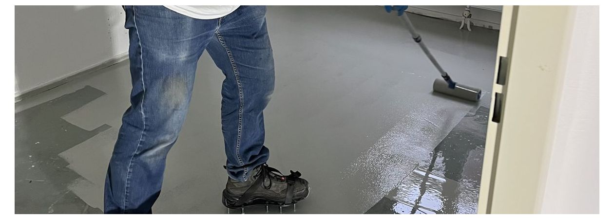 een persoon welke met een nylon roller vloercoating aanbrengt op de vloer.